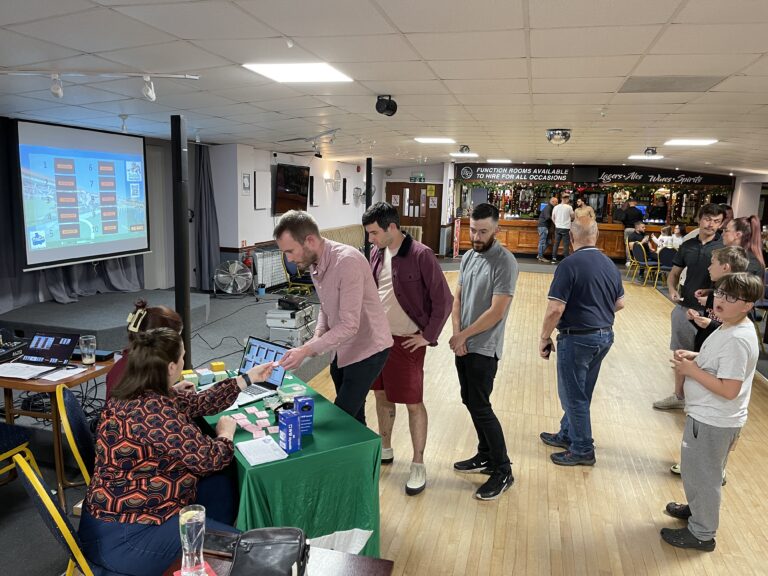 Guests buying tote tickets at a Sussex Race Nights fundraising event with the race board on screen