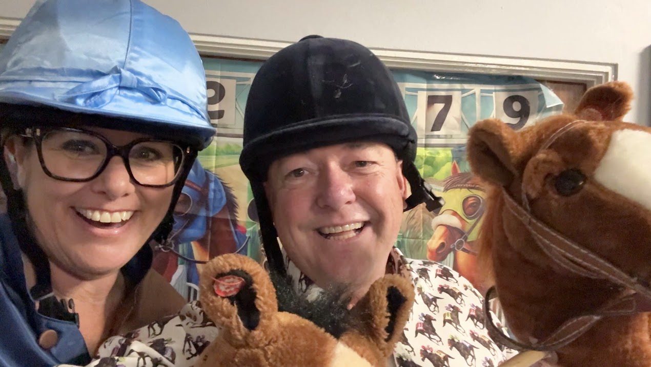 Two Sussex Race Nights hosts in jockey silks holding toy horses at a fundraising race night